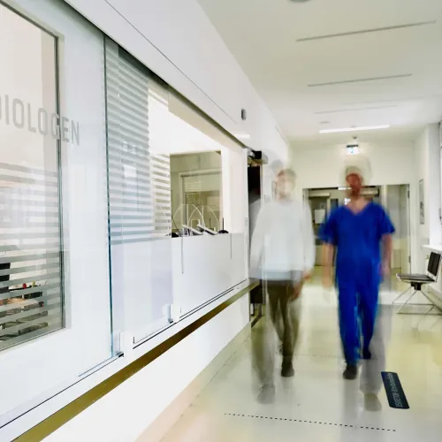 Flur mit Glasfront und vorbeigehendem medizinischem Personal.